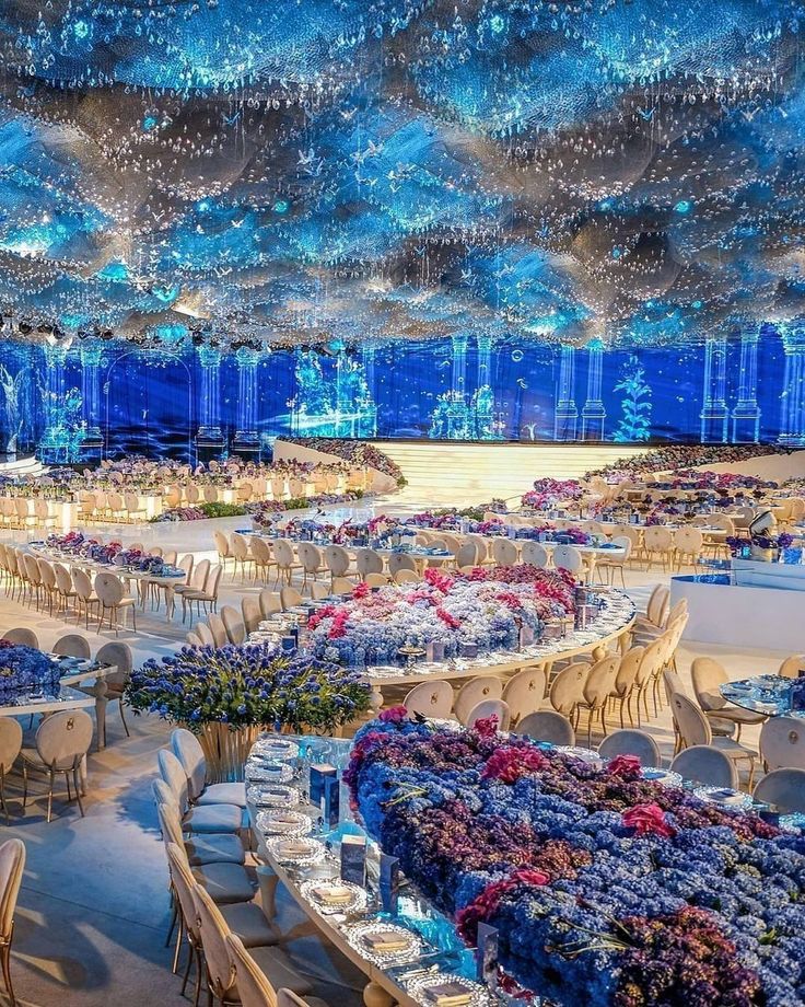 an elaborately decorated banquet room with blue lights and flowers on the tables, along with chandeliers hanging from the ceiling