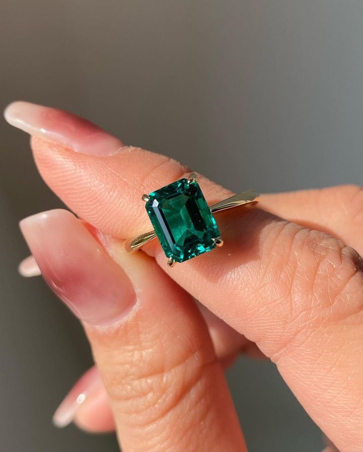 a woman's hand holding an emerald ring