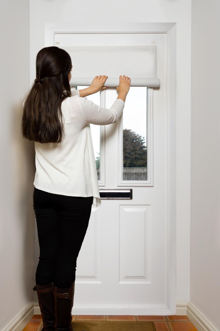 a woman standing in front of a white door opening a window with the blinds closed