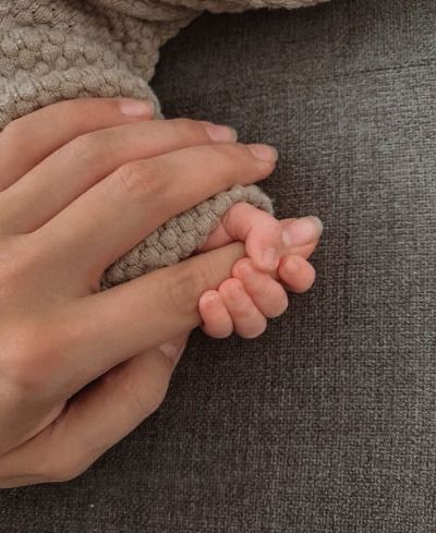 two hands holding a baby's hand with a heart on the other hand and a small red object in the background