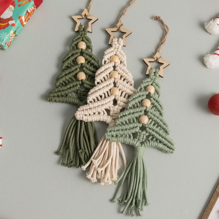 three crocheted christmas trees are hanging on a gray surface next to other holiday decorations