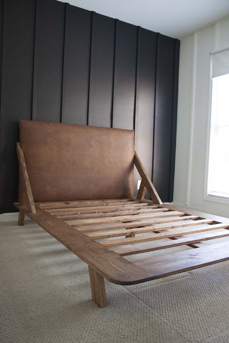 a bed frame made out of wood and leather is sitting in front of a window