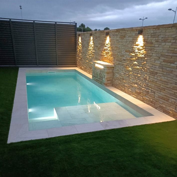 an empty swimming pool in the middle of a backyard with grass and lights on it