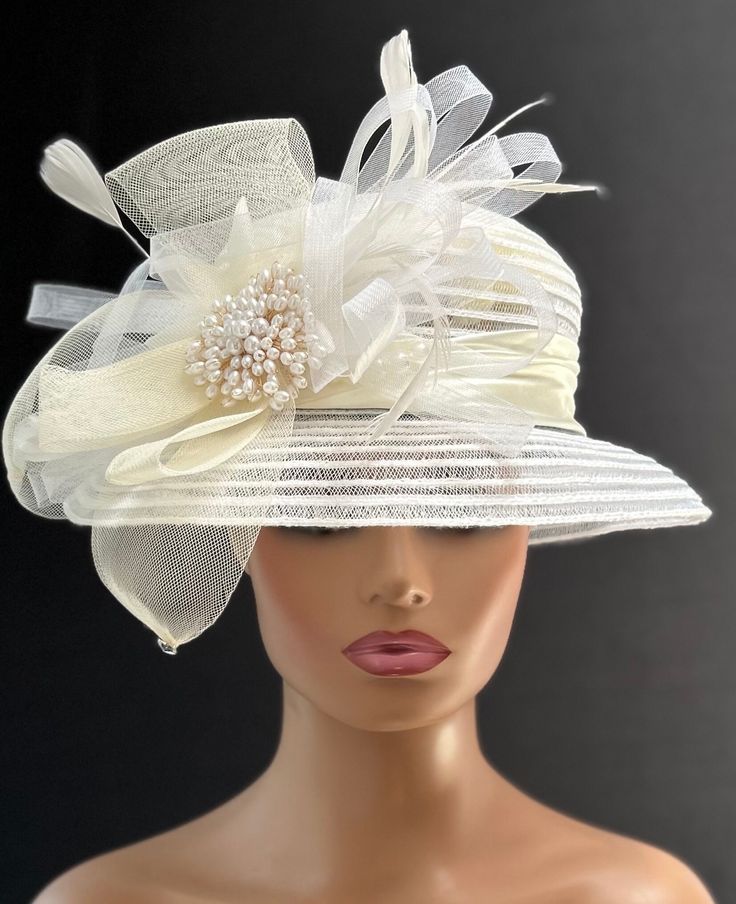 The hat featured here is an ivory and white lightweight linen and lace striped hat.  This is a one of a kind  hat  made by Letty. The hat is white with an ivory satin band. A crinoline design of white and ivory with several ivory feathers adorns the hat.  In the center of the crinoline design is a large cluster of off white pearls. Creating the look that suits you best can be achieved just by  turning the hat on your head creating a different look with each twist till you find the look you love.. This gorgeous  hat is a beautiful Church hat or a Kentucky Derby Hat.  Also perfect  for  an Easter Hat, Tea Party hat, Wedding Party Hat, Fancy Dress Hat, Retro Hat and other special occasions hat. Brim:   3" Rise:   3" Size:    22" Beige Cloche Hat For Wedding, Fitted Cream Cloche Hat For Wedding, Fitted Cream Hat For Vintage Events, Cream Gatsby Style Hat, Elegant Summer Hats For Mother Of The Bride, Elegant Summer Hat For Mother Of The Bride, Adjustable Cream Gatsby Hat, Cream Adjustable Gatsby Hat, White Vintage Fascinator Hat