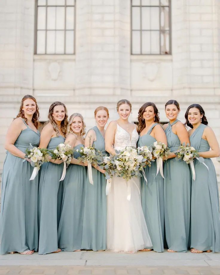 a group of women standing next to each other in front of a stone building holding bouquets