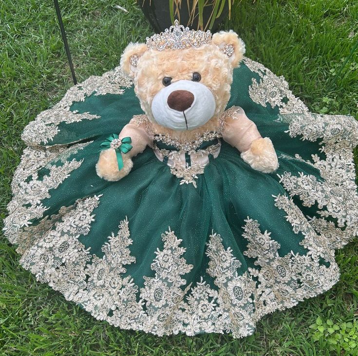 a teddy bear dressed in green and white sitting on the grass with a dress around it's neck