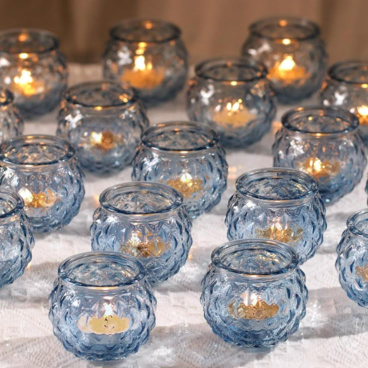 there are many small glass bowls with candles in them sitting on the tablecloth and next to each other