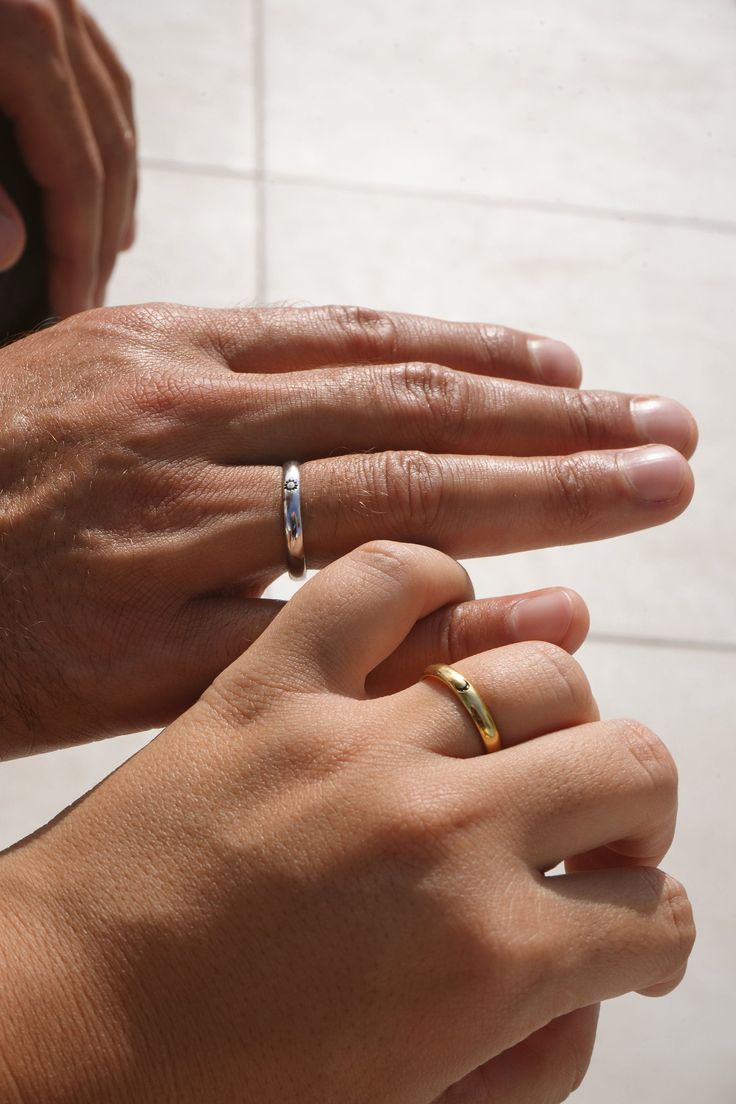 two people holding hands with wedding bands on their fingers, one wearing a diamond ring