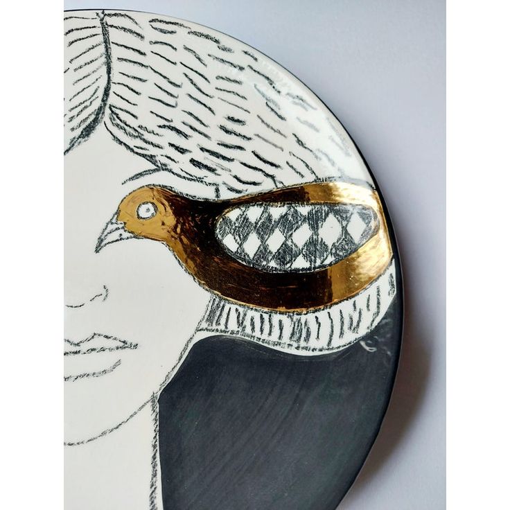 a white and gold plate with a bird on it's face in front of a gray background