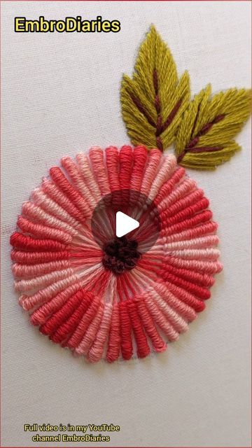 an embroidered flower with green leaves on the top and pink petals on the bottom, in front of a white background