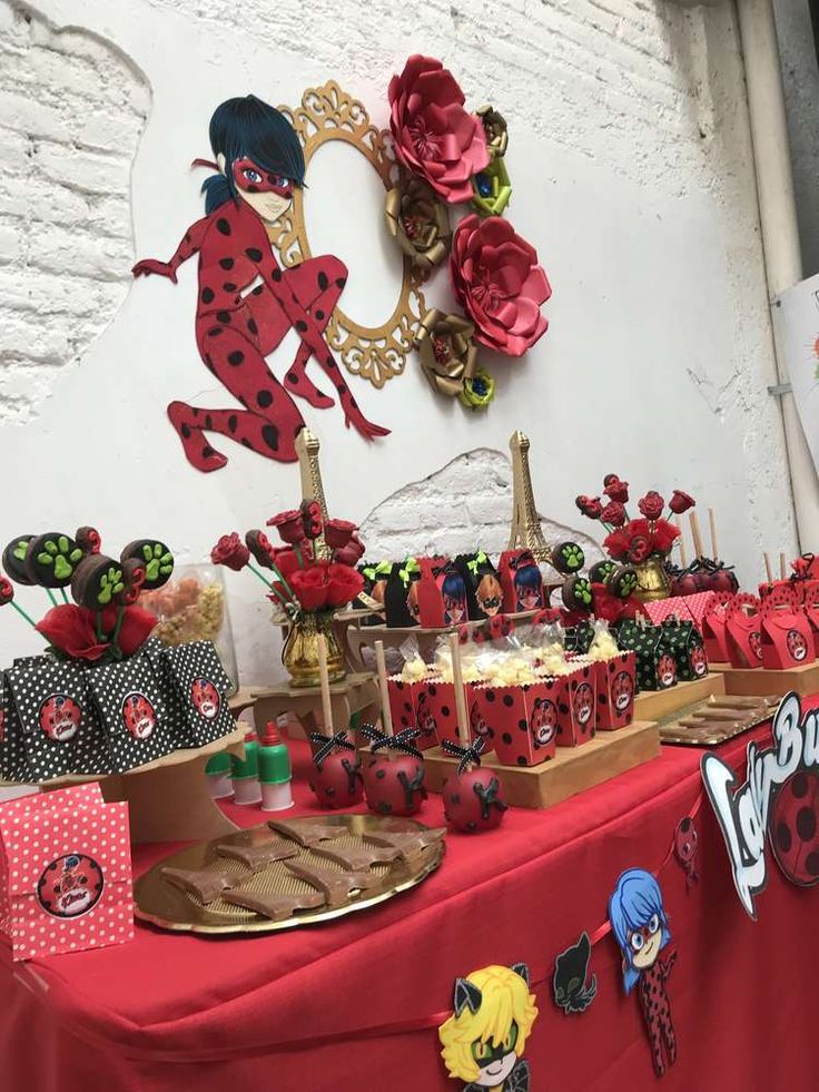 ladybug birthday party decorations and desserts displayed on a red table cloth covered buffet