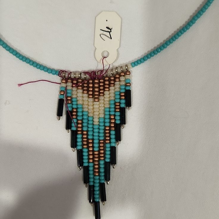 a beaded necklace is hanging on a white wall and has a tag attached to it