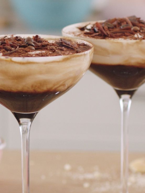 two martini glasses filled with chocolate dessert and topped with whipped cream, chocolate shavings