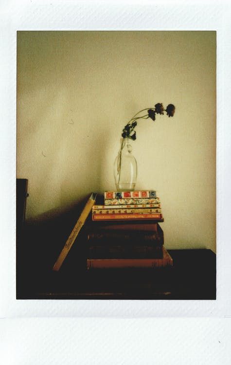 a stack of books sitting on top of a table next to a vase filled with flowers