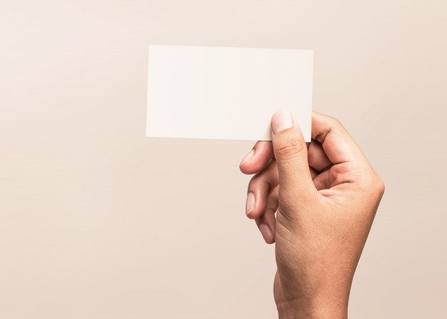 a person holding up a white business card in their right hand, against a beige background