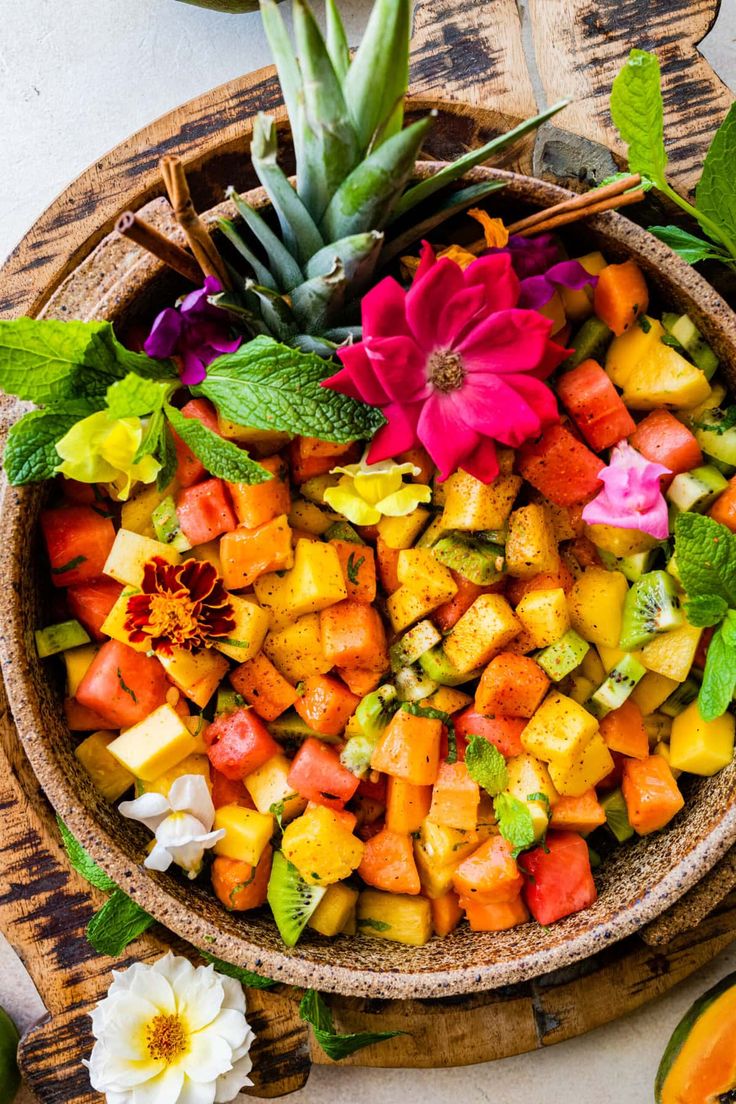 a bowl filled with fruit and flowers on top of a wooden table next to other fruits