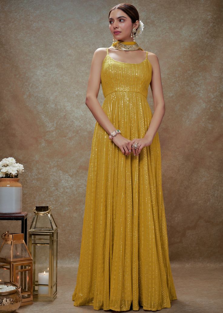 Shine effortlessly with this stunning Yellow and Gold Sequin Embroidered Anarkali Gown, crafted from a luxurious viscose georgette. The vibrant yellow anarkali features a chic strappy round neckline, exuding elegance with intricate sequin and threadwork embroidery that catches the light beautifully with every movement. A sophisticated back cutout at the waist adds a modern twist, perfectly balancing tradition with contemporary flair. The look is completed with a matching net dupatta adorned with delicate embroidered scallop lace, ensuring a flawless look. Ideal for Haldi, Mehndi, Sangeet events, or as an eye-catching wedding guest attire, this gown is designed to make you stand out effortlessly. Composition : Anarkali - Viscose Georgette and Dupatta - Soft net Care: Dry Clean Only and Vacu Designer Yellow Georgette Gown, Yellow Georgette Dress With Mirror Work, Yellow Georgette Gown For Diwali, Yellow Embellished Anarkali Set For Diwali, Yellow Fitted Anarkali Gown, Yellow Anarkali Set With Cutdana For Party, Elegant Yellow Navratri Dress, Gold Embellished Georgette Gown, Yellow Georgette Gown For Festive Occasions