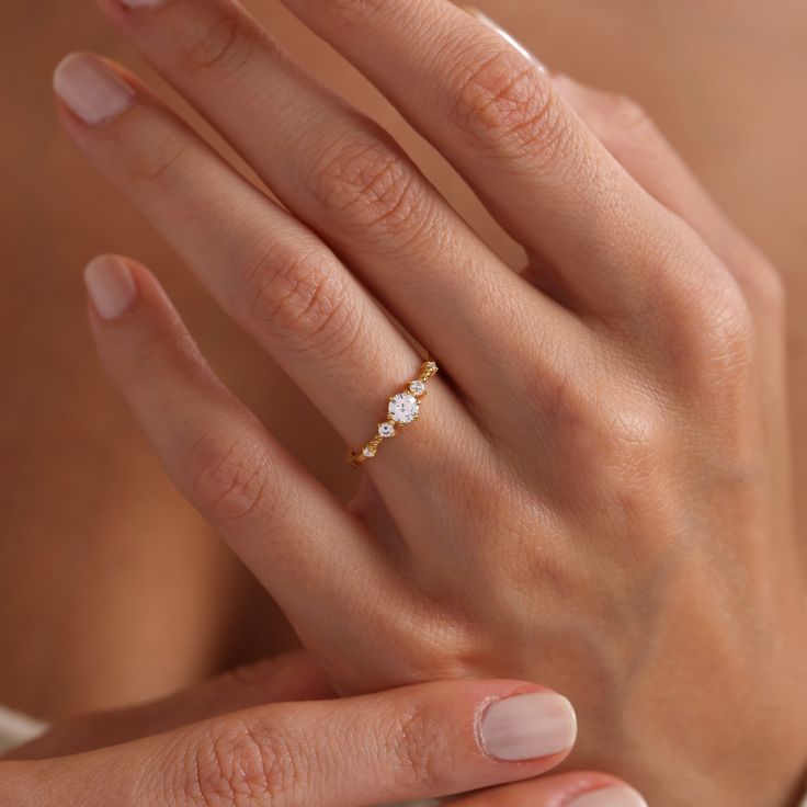 a woman's hand wearing a gold ring with three small white stones on it