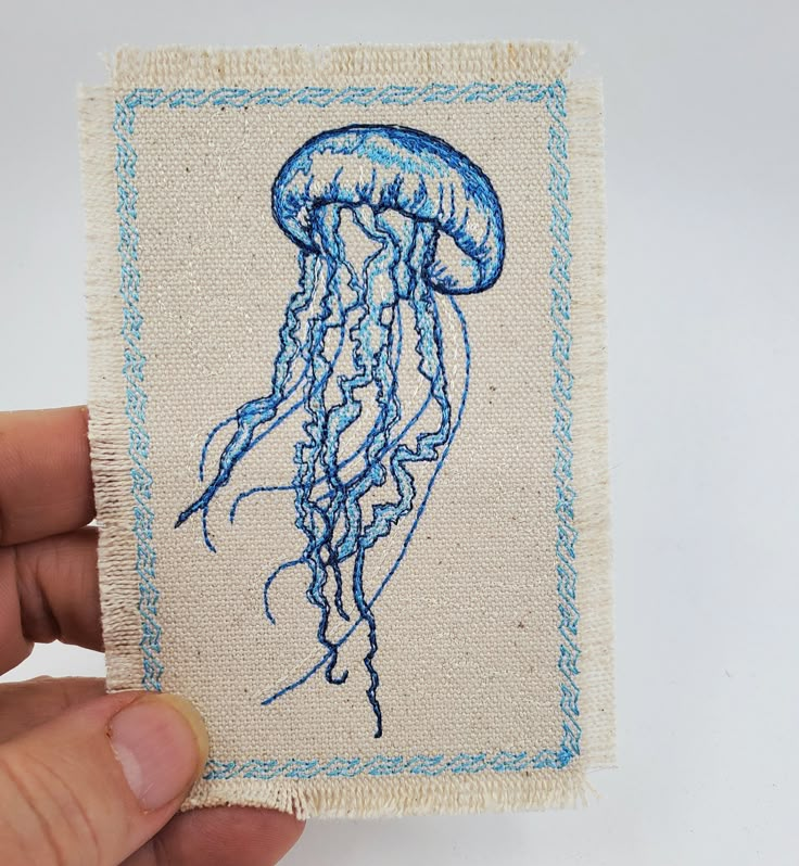 a hand holding up a piece of fabric with a drawing of a jellyfish on it