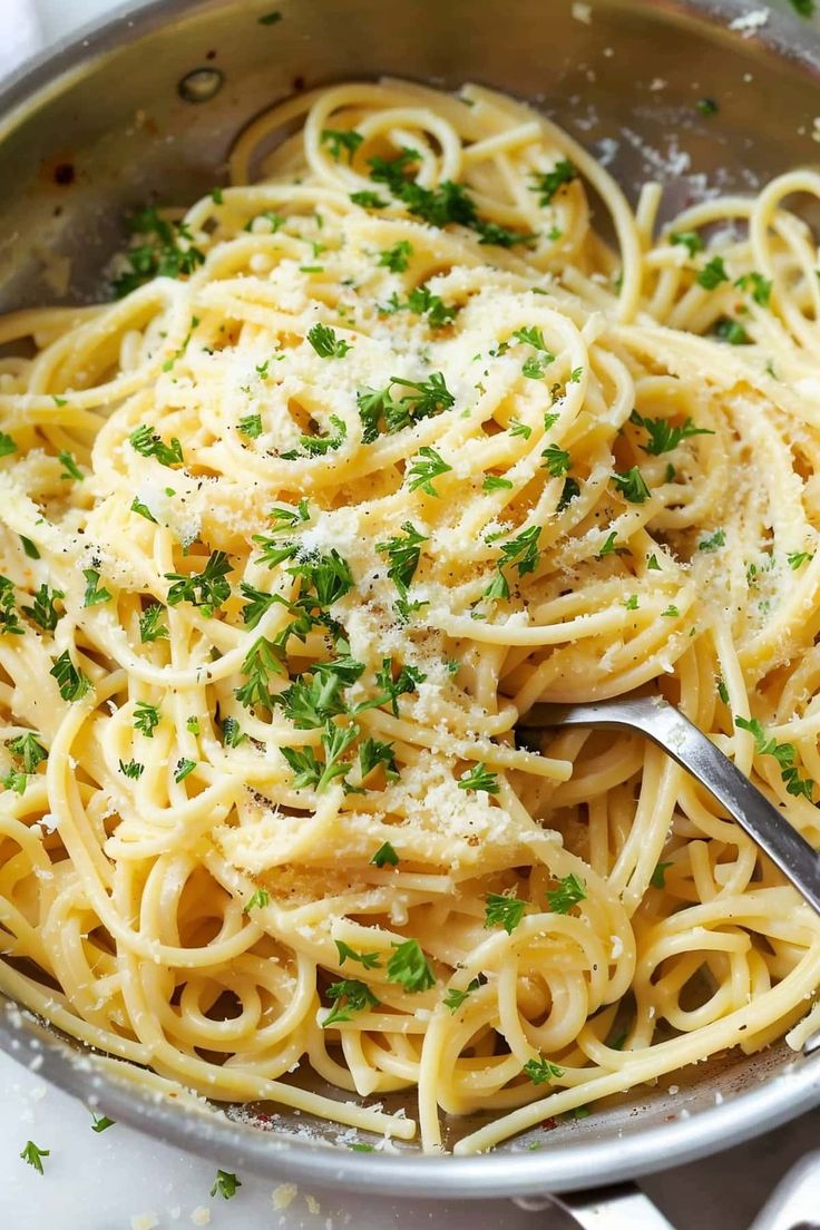 pasta with parmesan cheese and herbs in a silver bowl on a white table