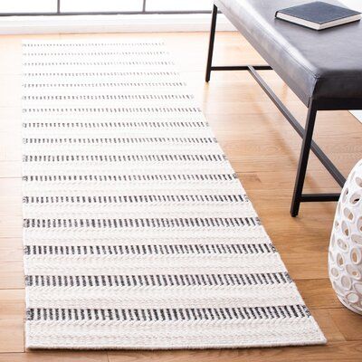 a white and black rug in a living room next to a bench with a book on it