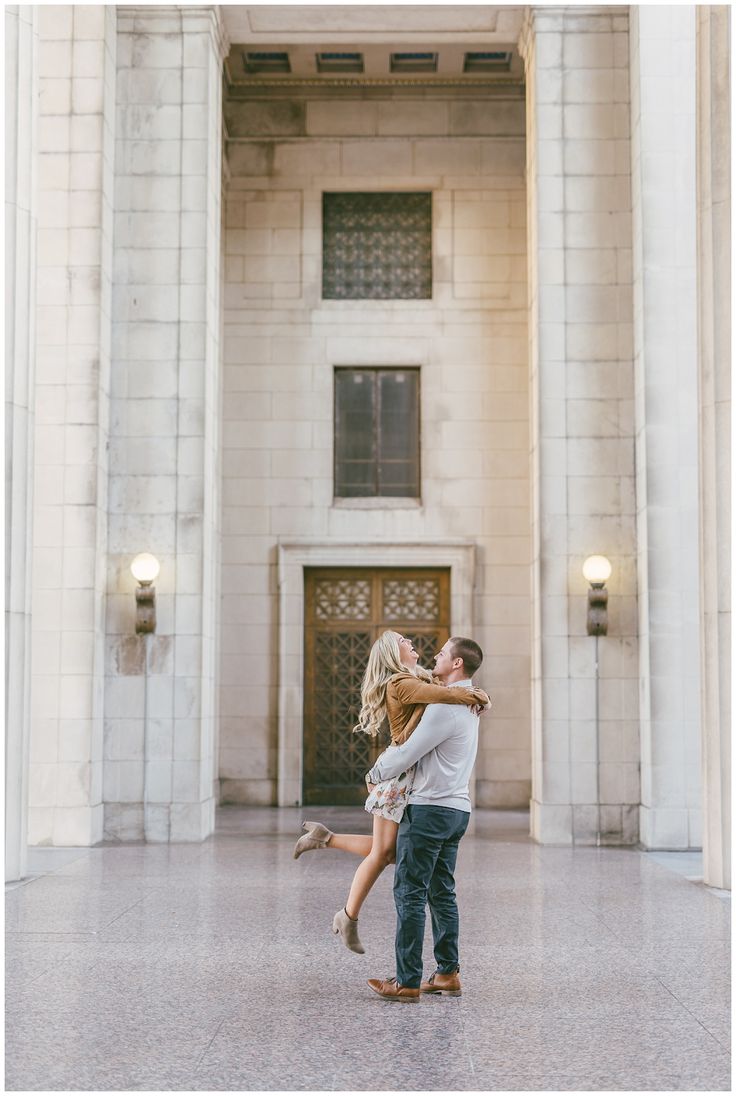 an engaged couple kissing in the middle of a large building with columns and doors on either side