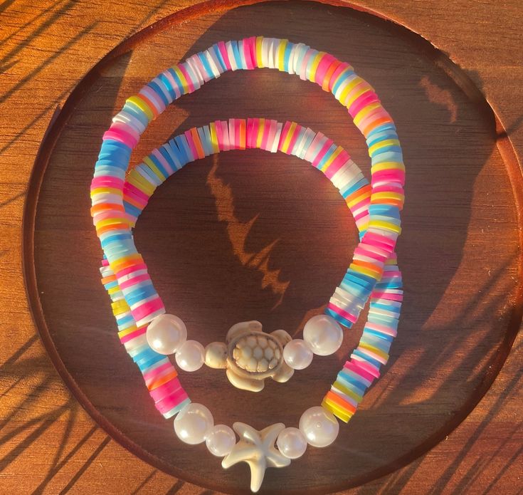 two bracelets with shells and beads on a table next to a shadow from the sun