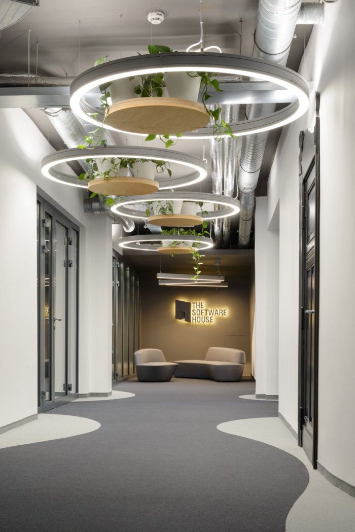 an office hallway with plants hanging from the ceiling and circular lights above it, along with couches