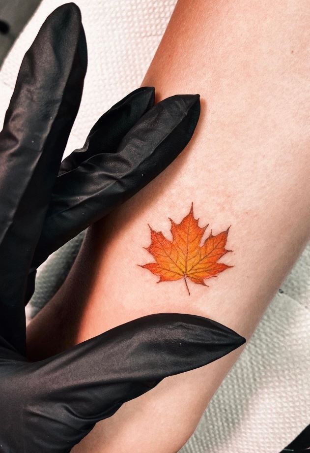 a woman's arm with an orange leaf tattoo on it