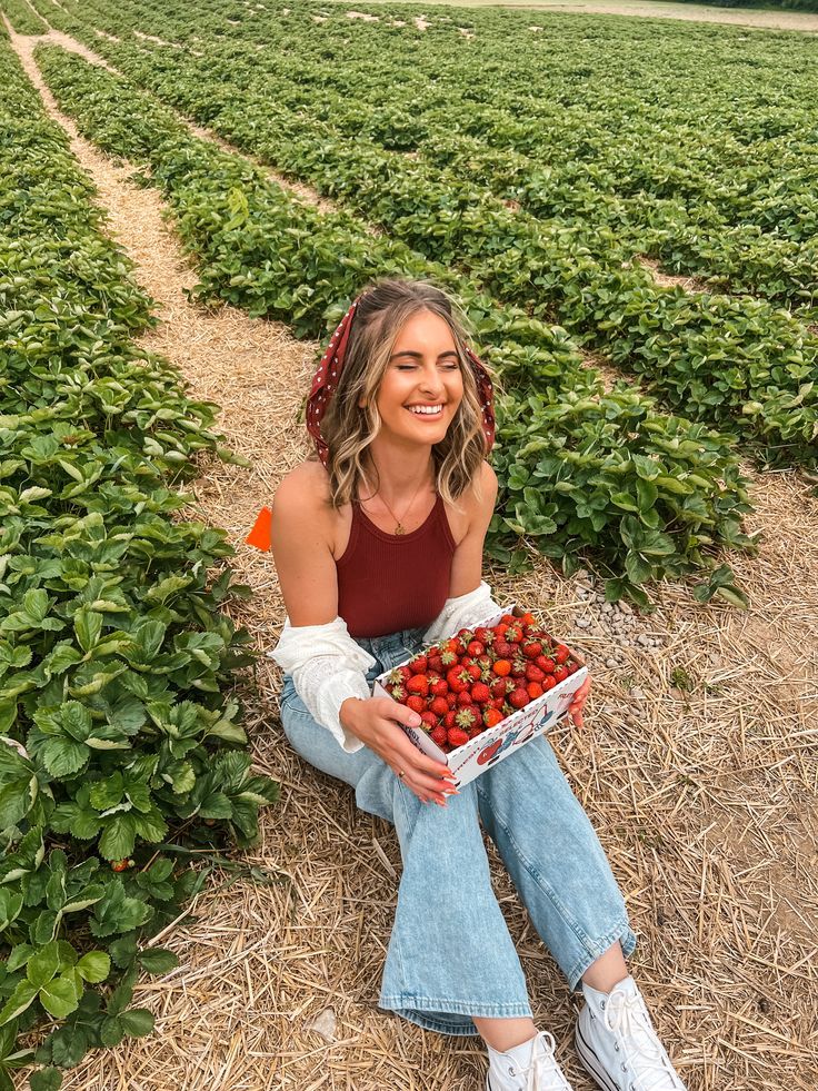 a woman sitting on the ground holding a box of strawberries in a strawberry field