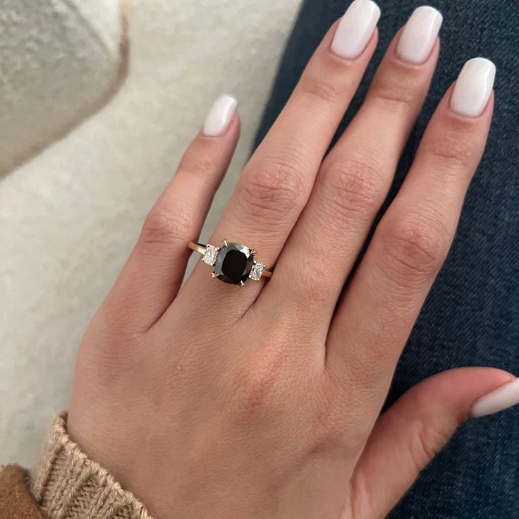 a woman's hand with white nails and a black diamond ring on her finger