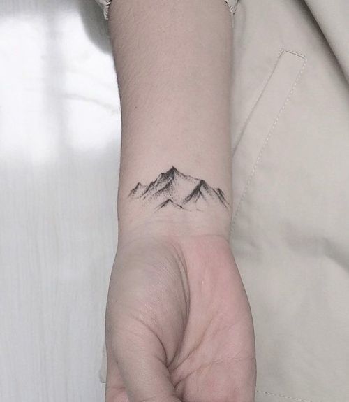 a person's hand with a mountain tattoo on the left side of their wrist