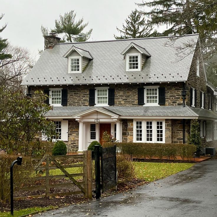 a large stone house with white windows and black shutters on the front door is shown