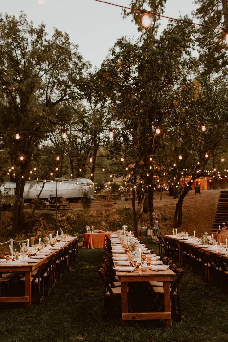 an outdoor dinner table set up with lights strung from the trees