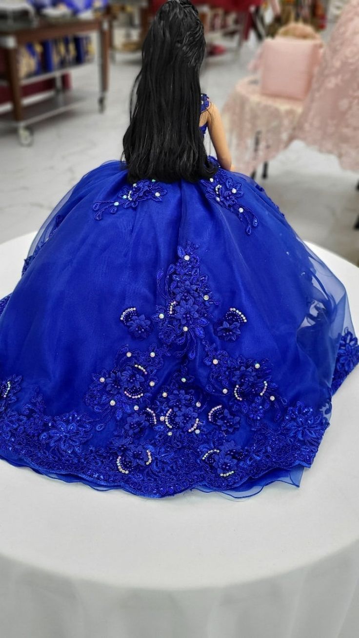 a doll sitting on top of a white table wearing a blue dress with beading