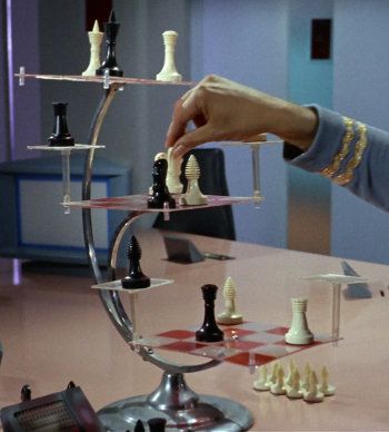 a person playing chess on a table with other pieces in front of them and one hand reaching for the queen's pawn