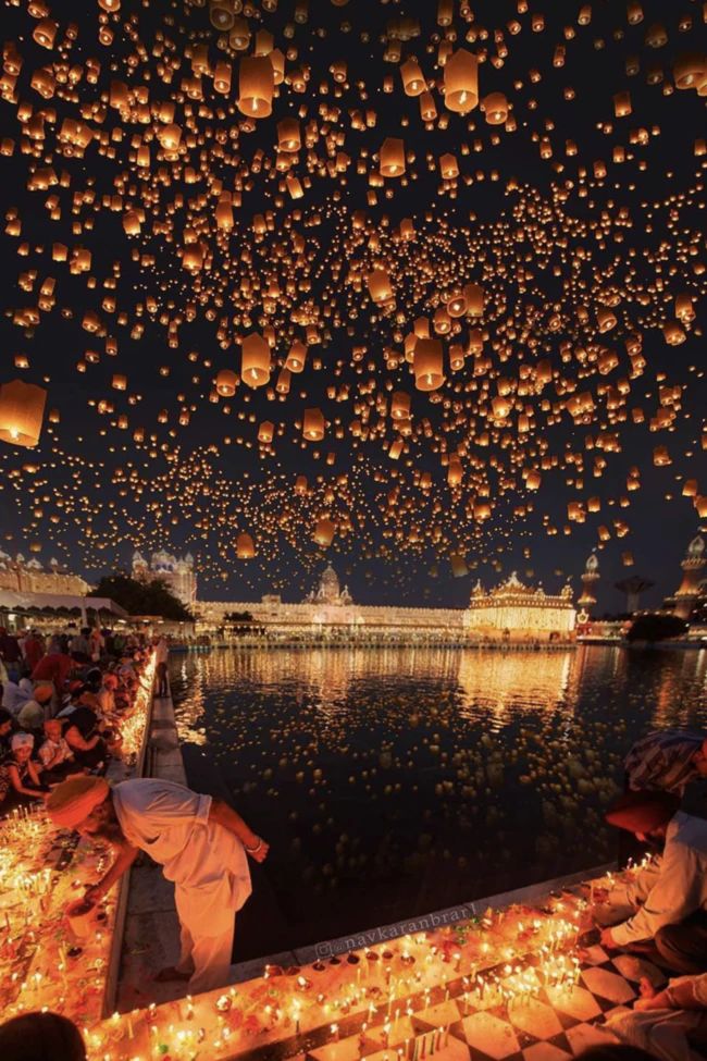 many people are sitting on the ground with lanterns floating in the air above them at night