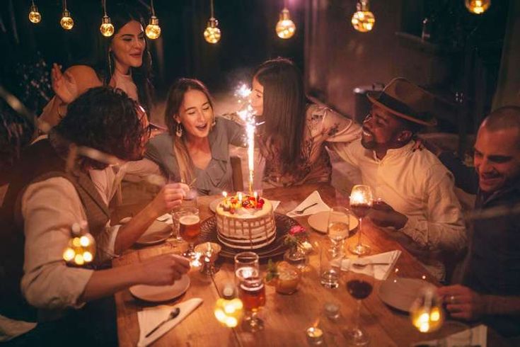 a group of people sitting around a table with a cake and candles in front of them