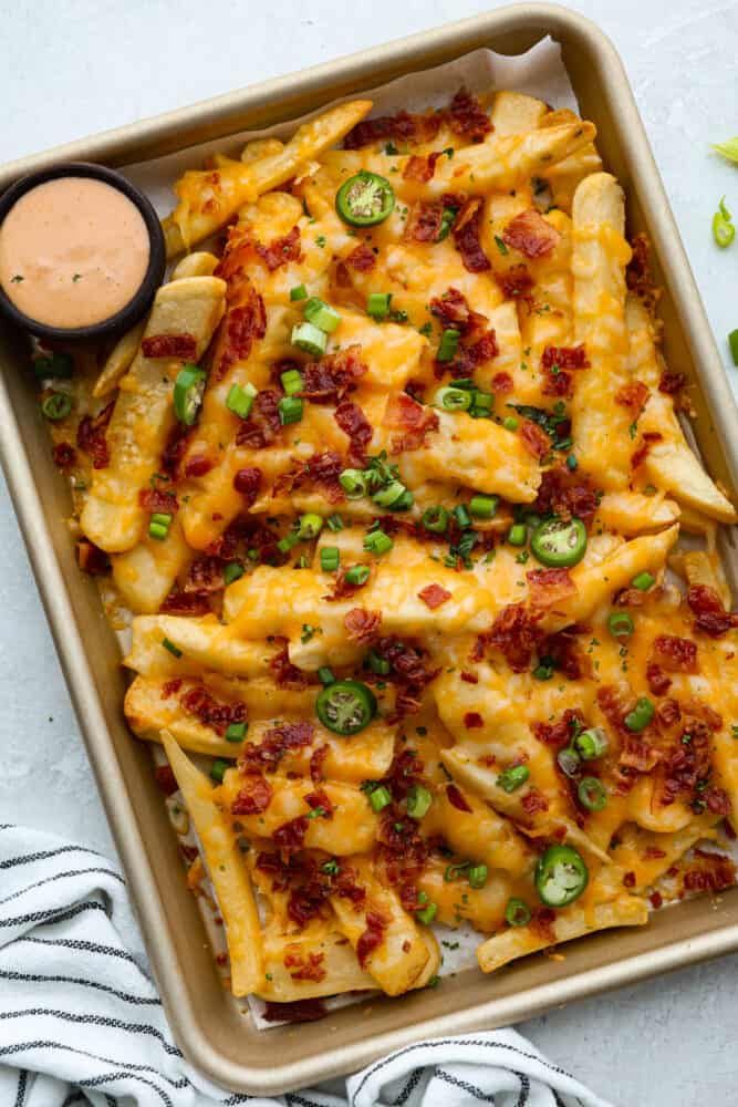 a casserole dish filled with cheesy pasta and green onions next to a dipping sauce