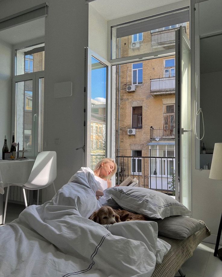 a woman laying in bed next to a window