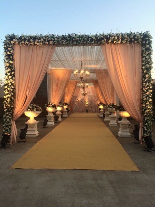 an outdoor ceremony with white and pink draping, candles and flowers on the aisle