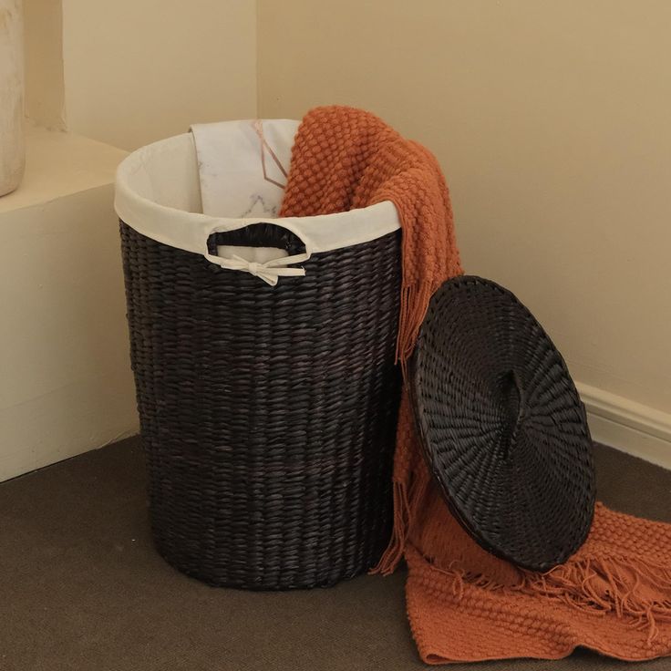 a black basket sitting on the floor next to an orange towel and a brown hat