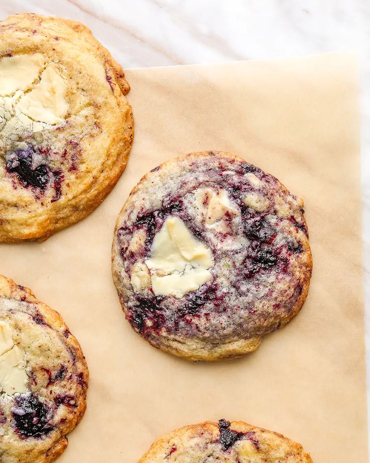 four blueberry muffins sitting on top of a piece of parchment paper