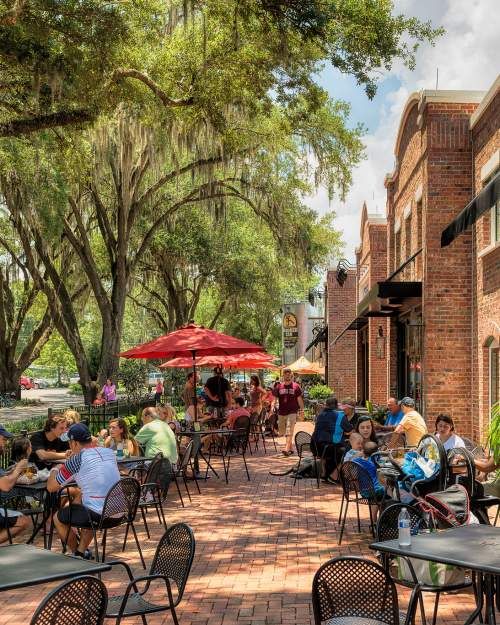 people are sitting at tables outside under umbrellas on the sidewalk in front of brick buildings