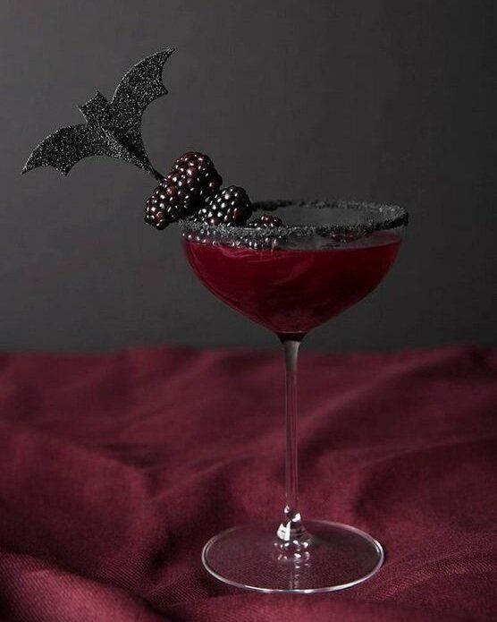 a red drink in a martini glass with a black bat garnish on top