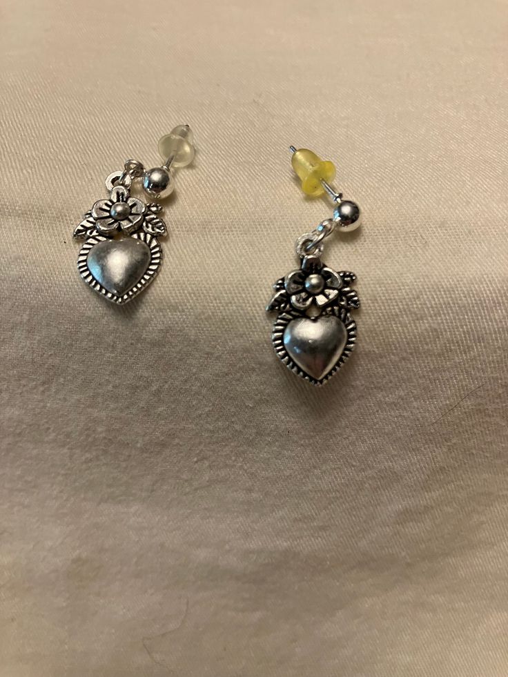 These dainty silver tone earrings consist of a 4mm ball post insertion stud with a little, one-sided 3D charm dangle. The charm shows a simple flower with a small heart below it. The earrings measure approximately 1 inch in length and come with butterfly backs. You can choose to add a drawstring gift bag for $1 in the dropdown.  Disclaimer: all measurements are approximate, as I only have a tactile tape measure that measures in half inches. Shades may vary based on lighting and your monitor. Colors were chosen with the assistance of friends and family or based on the description of the materials I bought. If you have an idea or request for a custom design, I will do my best to find materials and create your perfect item. I try to be accurate when listing my materials but I make no promises Heart Charm Dangle Jewelry For Gifts, Heart Charm Dangle Jewelry For Anniversary, Anniversary Heart Charm Dangle Jewelry, Anniversary Dangle Jewelry With Heart Charm, Minimalist Heart Charm Dangle Jewelry, Delicate Silver Heart Jewelry, Delicate Heart Shaped Silver Jewelry, Trendy Silver Flower Earrings For Pierced Ears, Hypoallergenic Drop Earrings For Valentine's Day