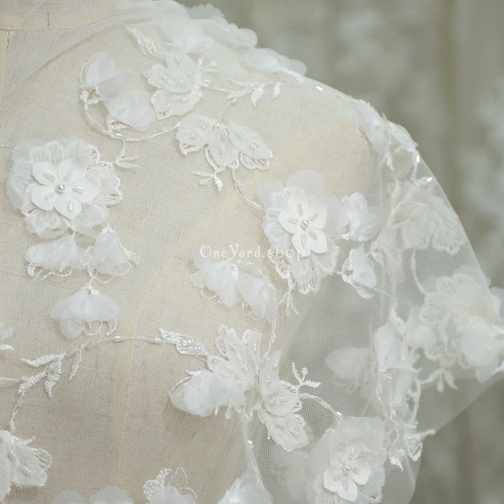 the back of a wedding dress with white flowers on it's lace and tulle