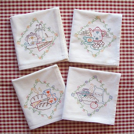 four embroidered napkins with designs on them sitting on a checkered cloth tablecloth