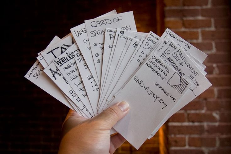 a person holding up several pieces of paper with writing on them in front of a brick wall