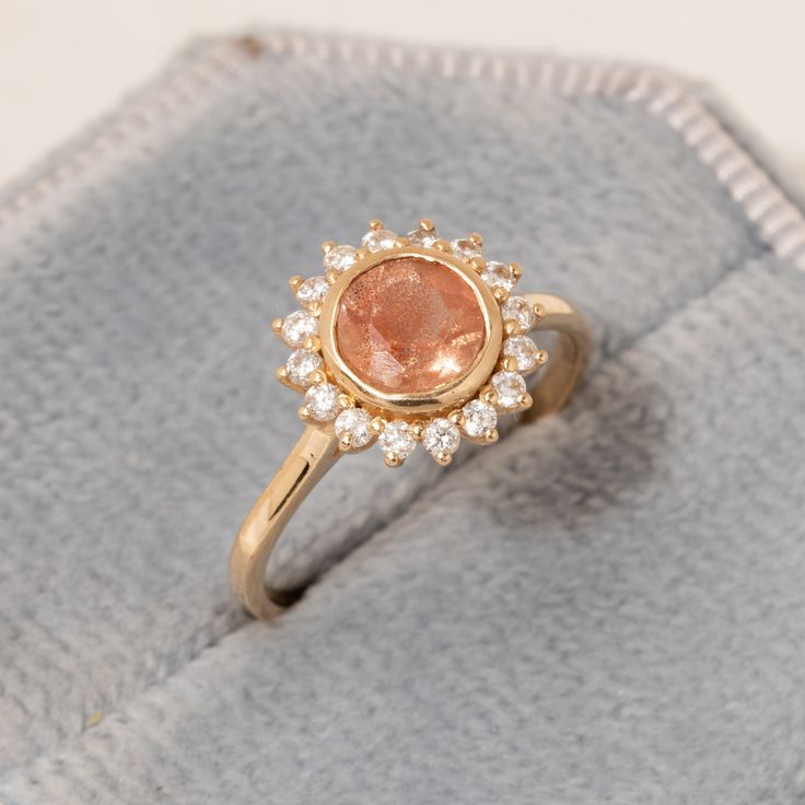 a gold ring with an orange stone surrounded by small white diamonds on a gray cloth